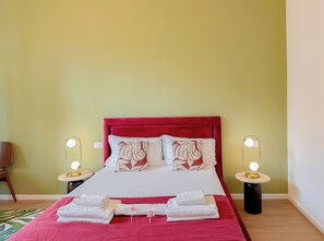 Ein ordentlich bezogenes Bett mit rotem Kopfteil, zwei Nachttischlampen und ein Paar Handtücher auf dem Bett.