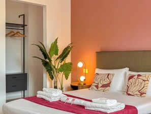 Ein Hotelzimmer mit einem Bett, einem Nachttisch mit Lampe, einer Pflanze und einem Kleiderschrank.