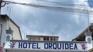 Ein Hotel namens 'HOTEL ORQUIDEA' mit heller Fassade, schwarzen schmiedeeisernen Fenstern und einer Tür sowie einem kleinen Balkon mit Blumendekoration.