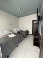Habitación de hotel con dos camas, un televisor de pantalla plana montado en la pared y una puerta que da a otra habitación.