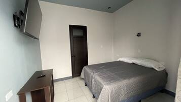 Un dormitorio con cama, escritorio, televisor montado en la pared y una puerta.