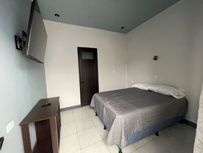 Un dormitorio con cama, escritorio, televisor montado en la pared y una puerta.