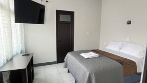 Ein Schlafzimmer mit einem Bett, einem Schreibtisch, einem Fernseher und einer Tür.