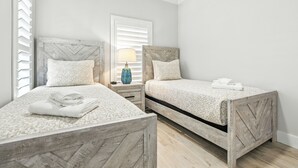 Um quarto com duas camas, uma mesa de cabeceira com abajur e uma janela com persianas.