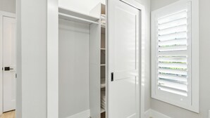 Um quarto com uma porta branca, um armário com prateleiras e uma janela com persianas.