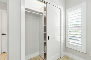 Ein Zimmer mit weißer Tür, einem Schrank mit Regalen und einem Fenster mit Jalousien.