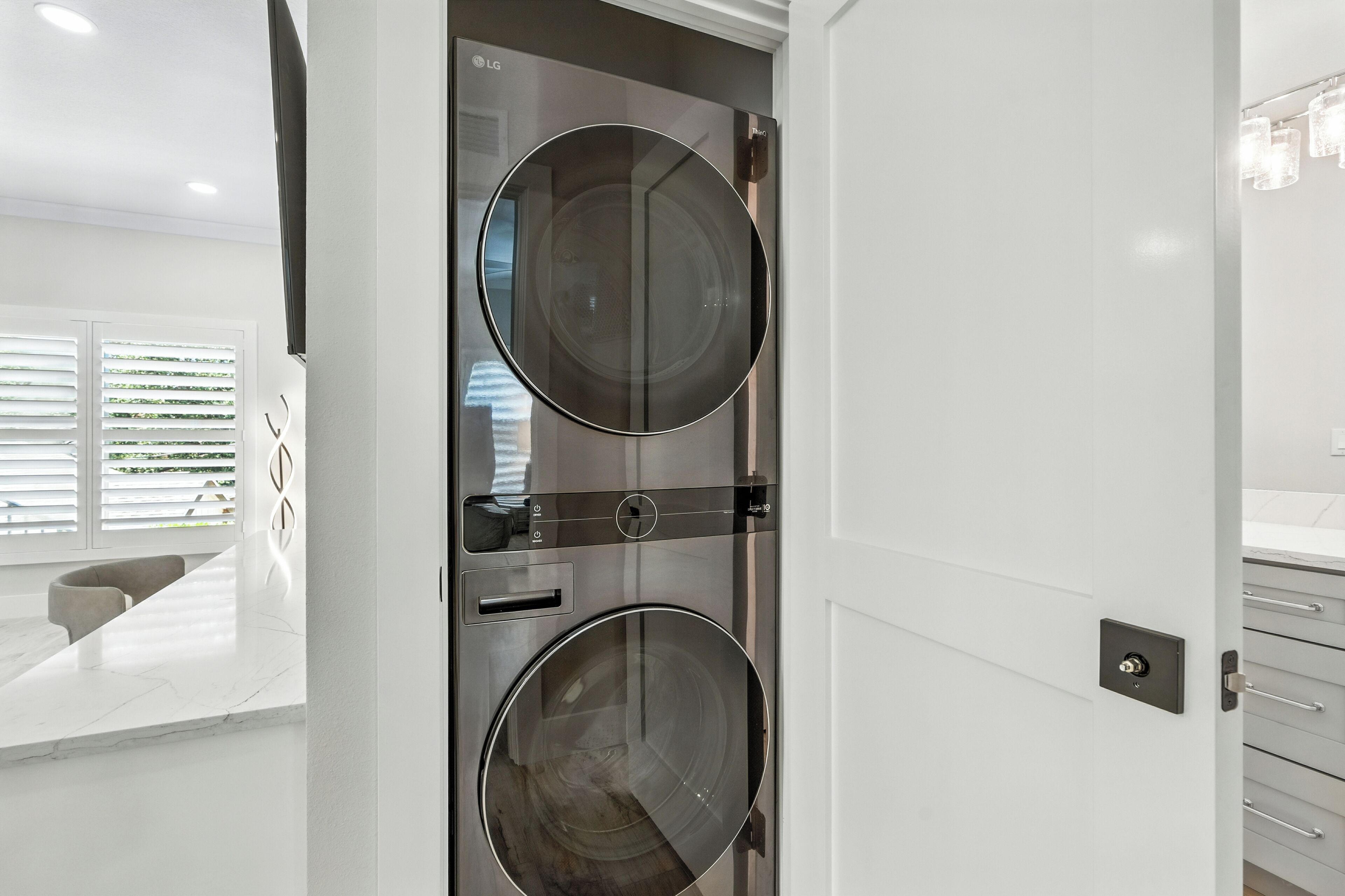 A modern, minimalist bathroom with a double-door washing machine and a sleek, white vanity.