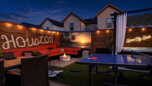 An outdoor patio with a ping pong table, a sofa, and a fire pit. - Space City House | Hot Tub + Cinema | Sleep 16+ (Houston)