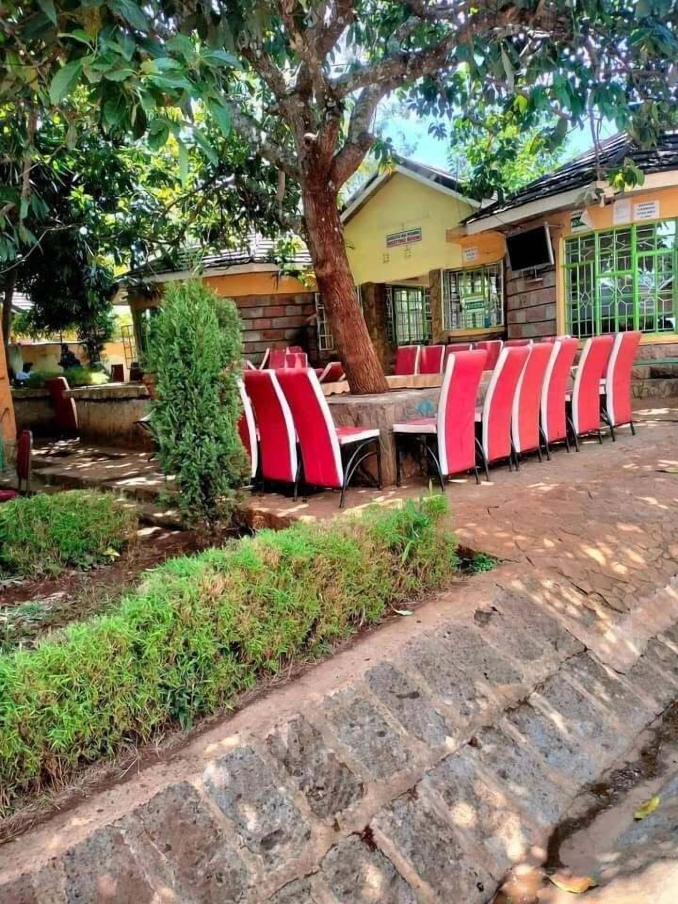 An outdoor seating area with red chairs and a table, surrounded by greenery and a stone pathway.