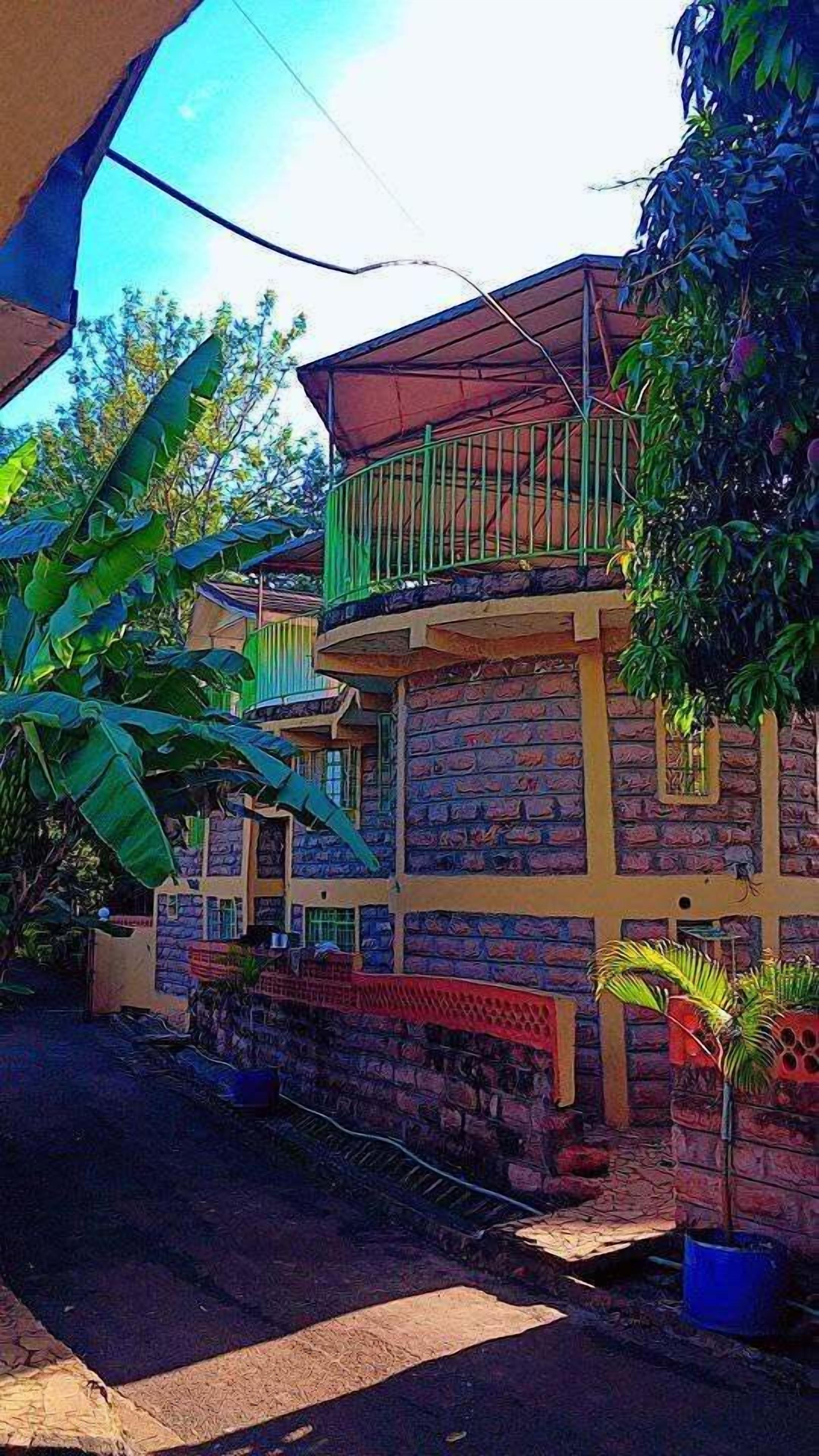 A two-story building with a balcony, surrounded by vegetation.