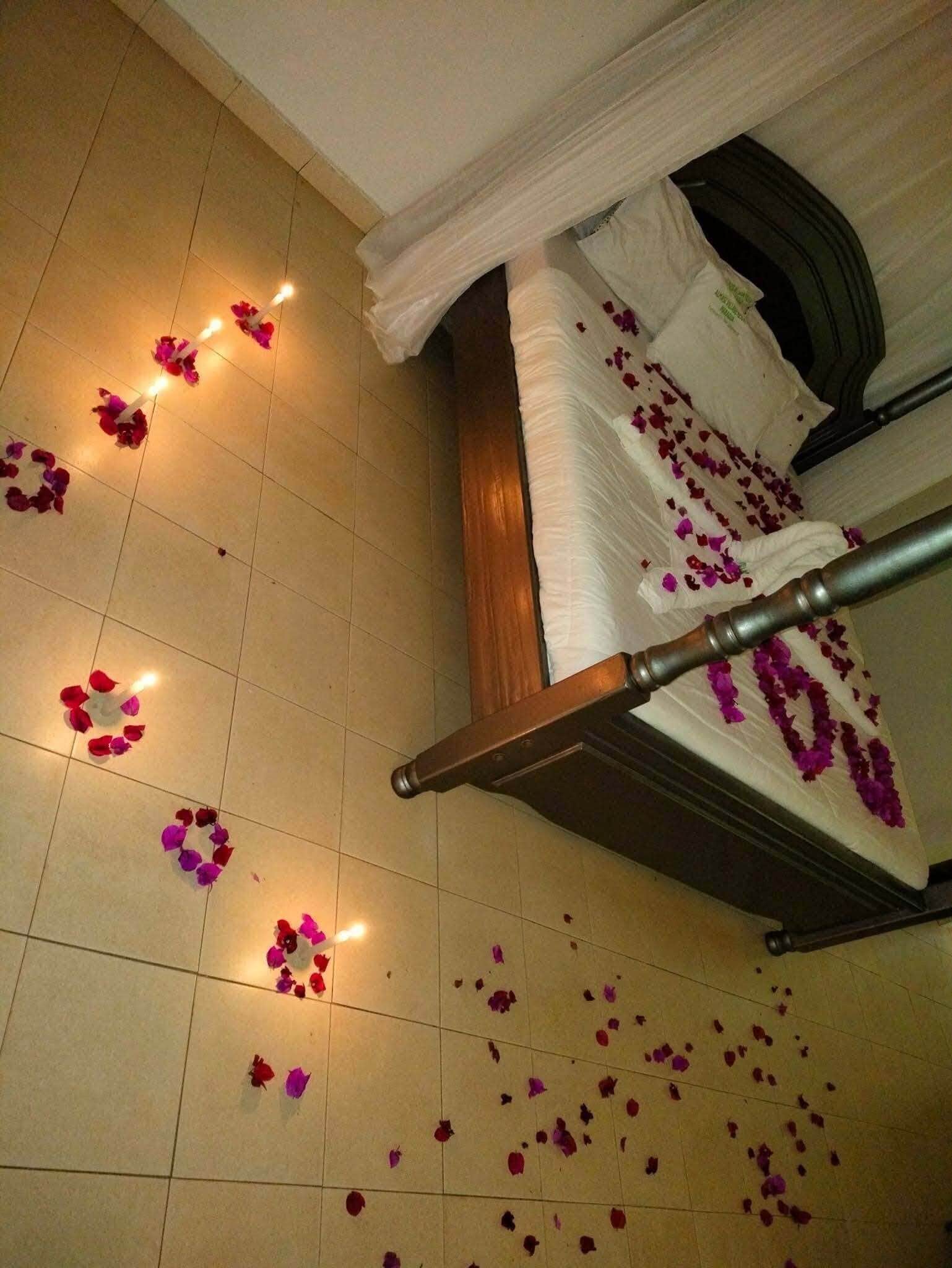A bed with a canopy, surrounded by scattered rose petals and small candles on the floor.