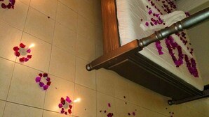 En seng med baldakin, omgivet af spredte rosenblade og små lys på gulvet.
