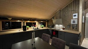 Eine moderne Küche mit Holzboden und -wänden, einem Essbereich mit Tisch und Stühlen sowie einer kleinen Kochinsel mit Spüle.