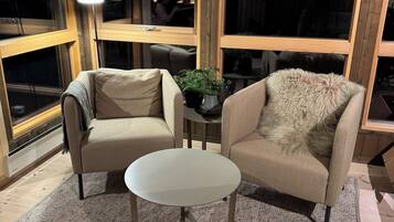 Una habitación acogedora con dos sillones color beige, una mesita blanca y un ventanal grande.