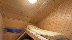 A compact wooden cabin room with bunk beds, a window, and a circular light fixture.