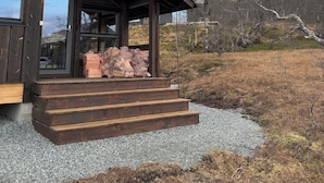 A wooden cabin with a porch and a stack of firewood outside.