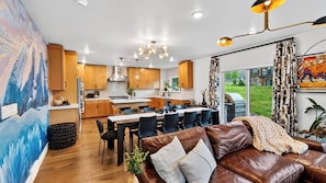 A modern kitchen with wooden cabinets, a dining area with a table and chairs, and a living room with a leather sofa.
