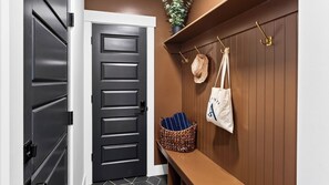 A hallway with a black door, a brown wall, and a shelf with bags and a basket.
