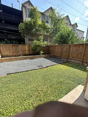 A residential backyard with a wooden fence, a grassy lawn, and a paved area with a drainage grate. - Cozy 1-bedroom apartment 4 mins from galleria mall Houston location (Houston)