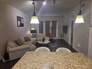 Ein modernes Wohnzimmer mit einer Couch, einem Esstisch und einer Küchenzeile im Hintergrund.