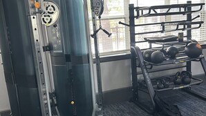 A gym with a squat rack, bench press, and weightlifting equipment. - Cozy 1-bedroom apartment 4 mins from galleria mall Houston location (Houston)