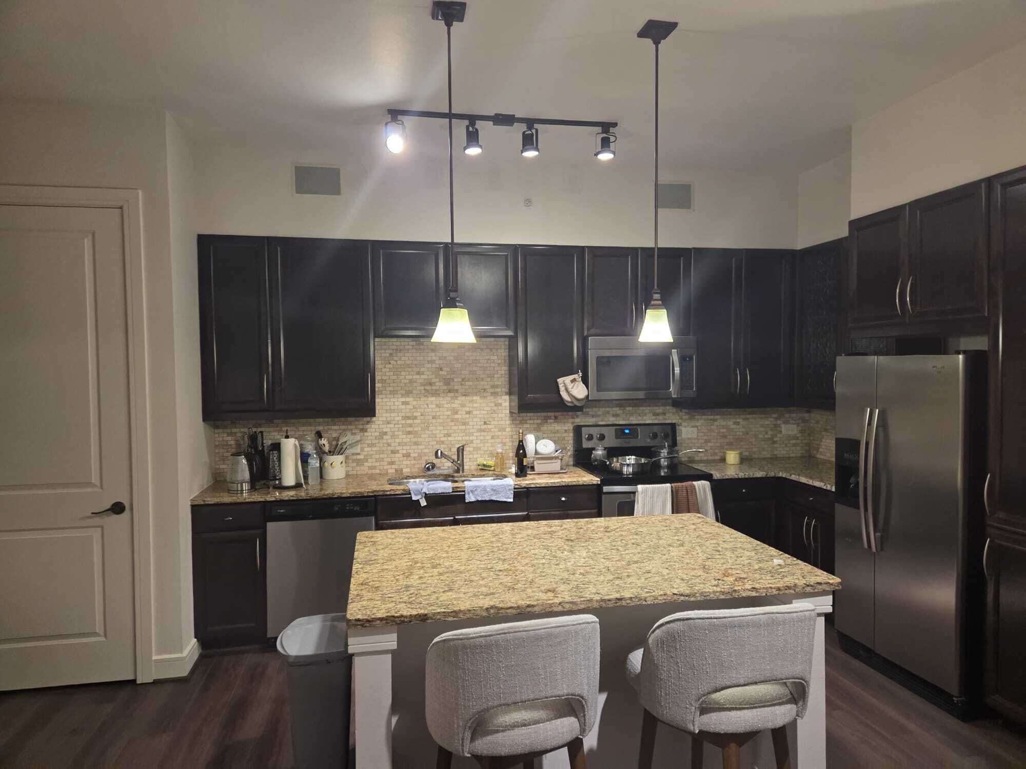 A modern kitchen with dark cabinets, a granite countertop, stainless steel appliances, and pendant lighting.