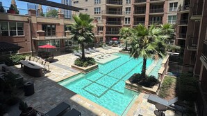 A rooftop pool area with lounge chairs, palm trees, and a view of a multi-story building. - Cozy 1-bedroom apartment 4 mins from galleria mall Houston location (Houston)