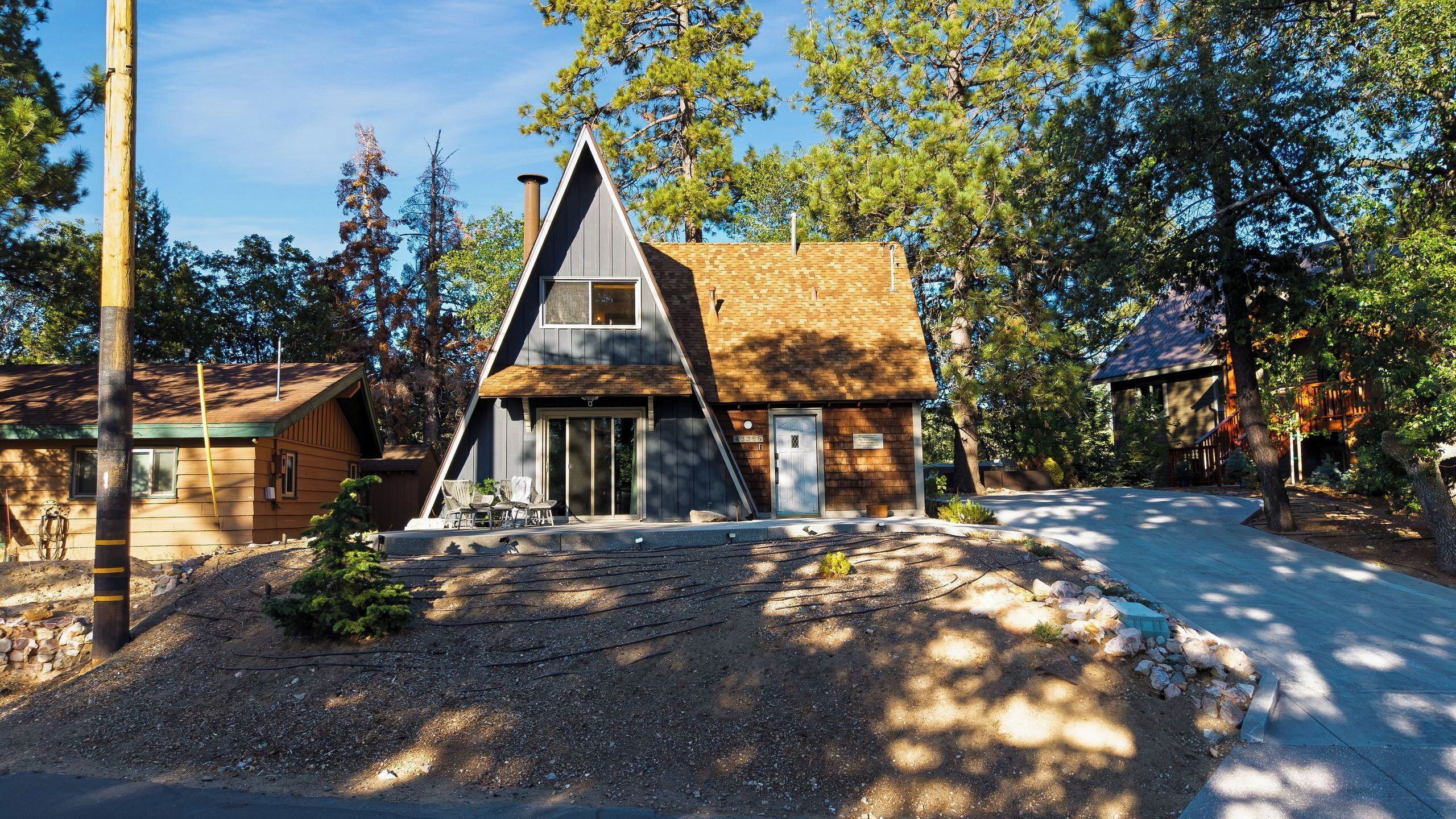 A two-story house with a steeply pitched roof, a front porch, and a driveway leading to a parking area.