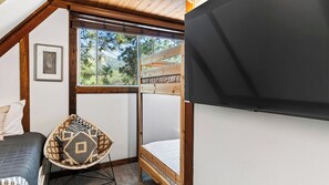 A bedroom with a bed, a chair, a window, and a wall-mounted TV. - A Big Bear View by Avantstay Classic A-frame Hot Tub Deck Fireplace Near Slopes & Marina (Big Bear Lake)