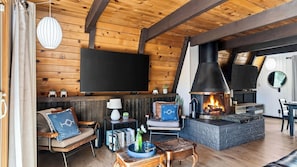 A cozy living room with a fireplace, wooden walls, a flat-screen TV, and comfortable seating. - A Big Bear View by Avantstay Classic A-frame Hot Tub Deck Fireplace Near Slopes & Marina (Big Bear Lake)