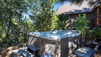 A hot tub with a wooden exterior, surrounded by trees and a house in the background.