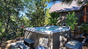 A hot tub with a wooden exterior, surrounded by trees and a house in the background.