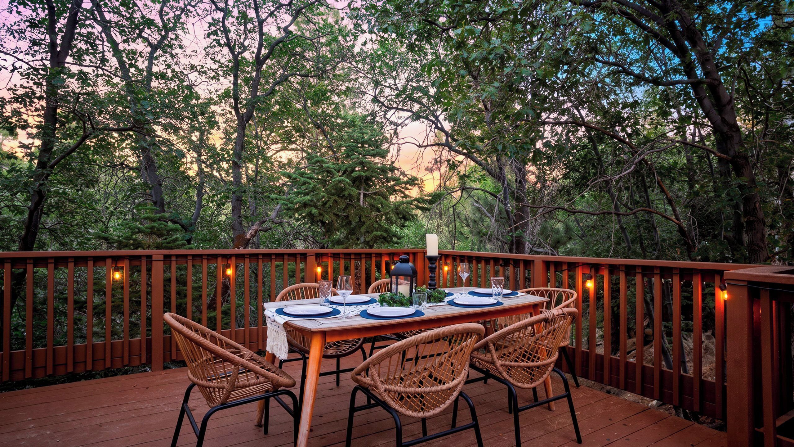 An outdoor dining area with a wooden deck, wicker chairs, and a table set for four.