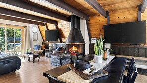 A cozy living room with a fireplace, wooden beams, a sofa, and a dining area.