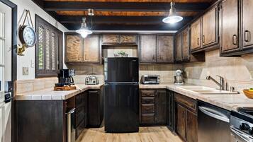 Una cocina con armarios de madera, un refrigerador negro, un tostador y un lavamanos.