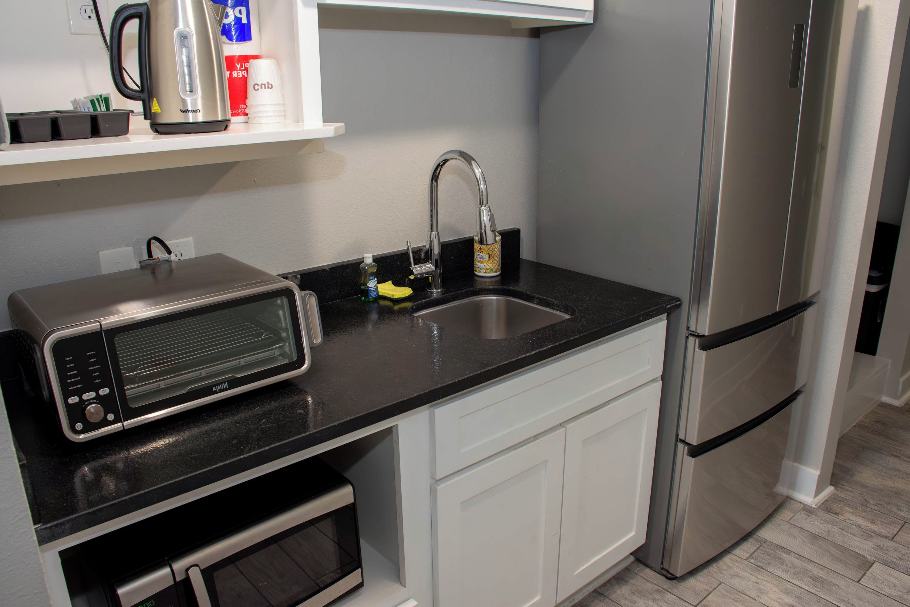 Una cocina con microondas, hervidor, lavamanos y refrigerador.