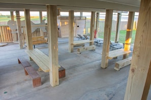 A covered outdoor area with wooden benches and picnic tables, a wooden deck, and a view of the beach.