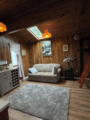A cozy room with a wooden ceiling, a sofa, a coffee table, a rug, a picture frame, and a small cabinet.