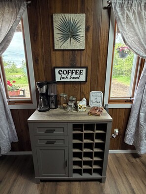 Una cocina con estación de café, un cartel que dice 'COFFEE' café recién hecho, y vista a espacios verdes.