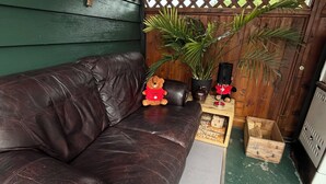 A dark brown leather sofa with a cushion, a small potted plant, a teddy bear, and a wooden crate.