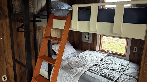 A bunk bed with a ladder, a shelf unit, and a window with a view.