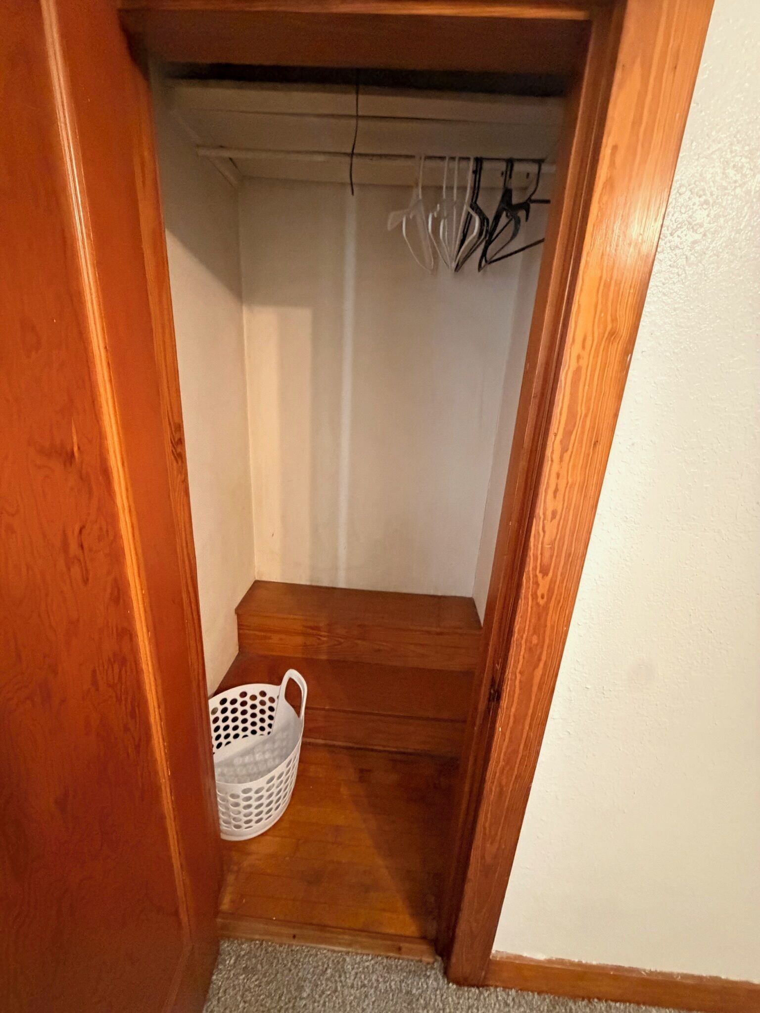 Una stretta scala in legno conduce a un pianerottolo con un cesto bianco sul pavimento.