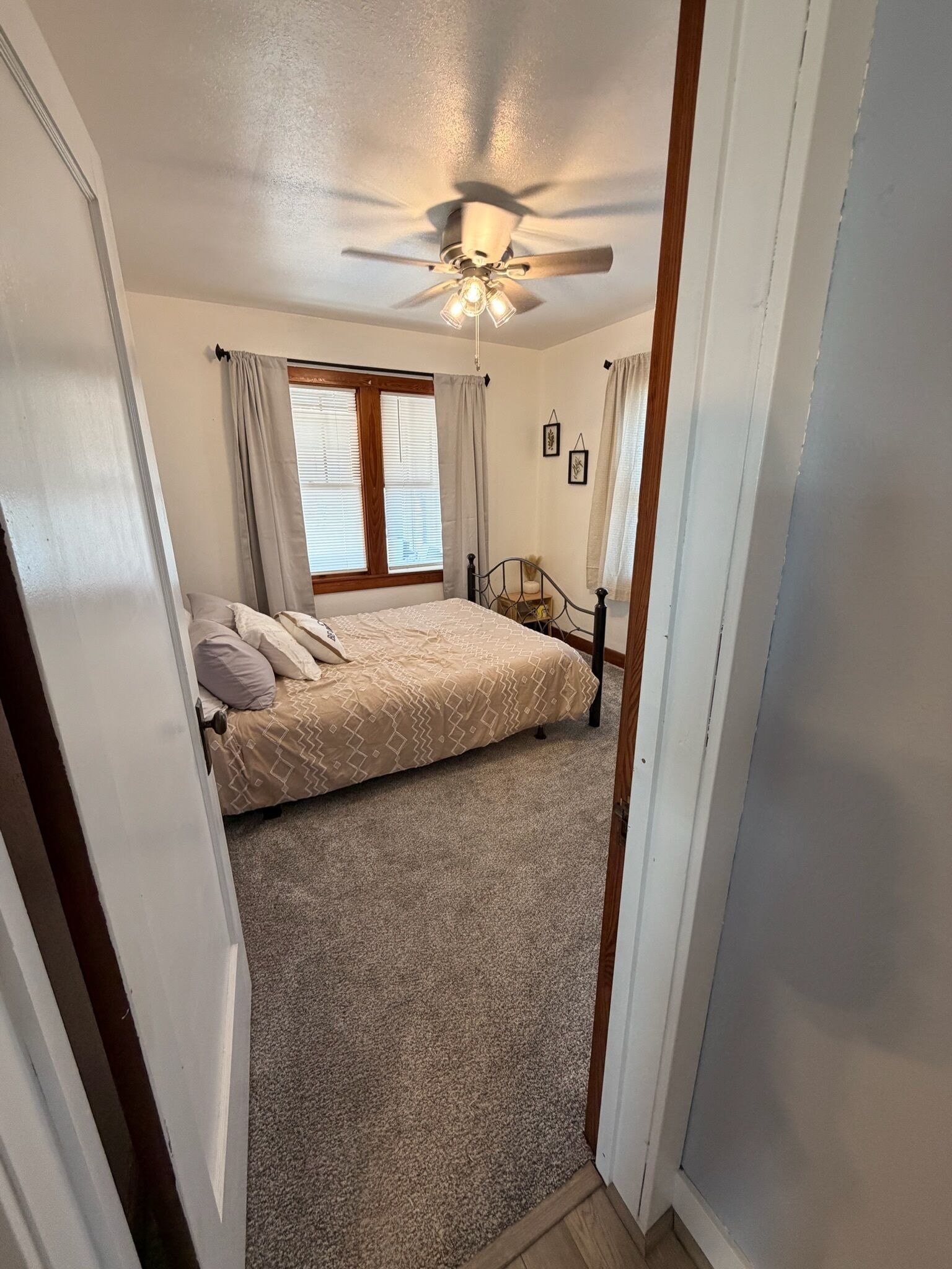 A bedroom with a bed, a ceiling fan, a window with curtains, and a nightstand with a lamp.