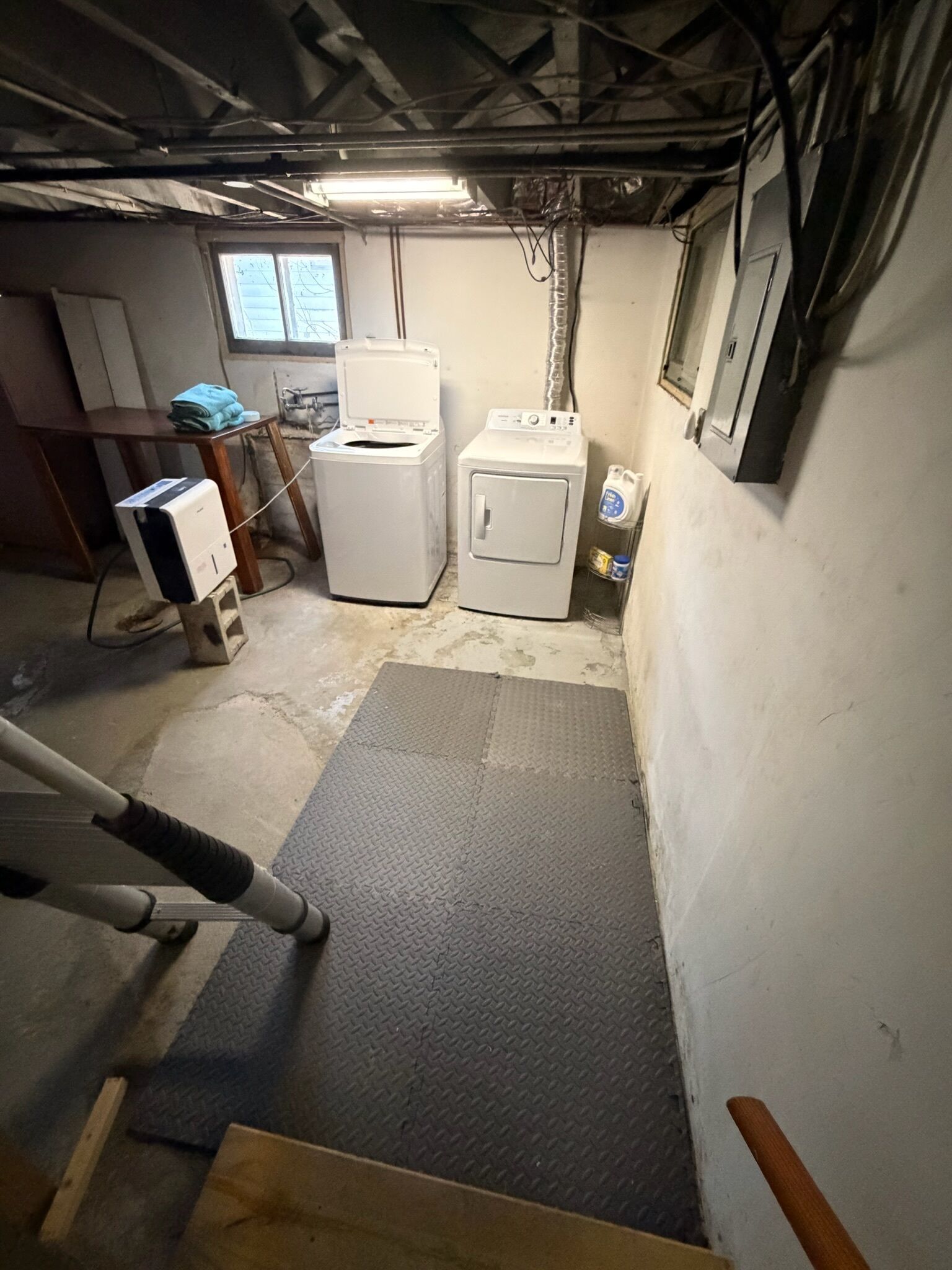 A laundry room with two washing machines, a drying rack, and a mat on the floor.