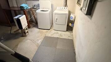 A laundry room with two washing machines, a drying rack, and a mat on the floor.