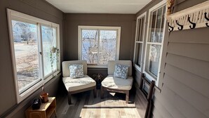 A sunlit room with two cushioned seating areas, large windows, and a wooden floor.