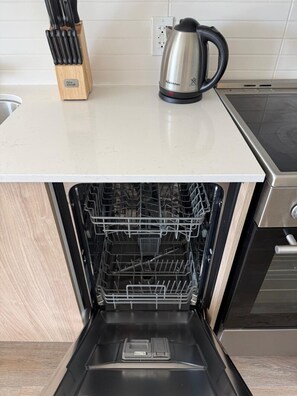A kitchen with a stainless steel kettle, a knife block, and an open dishwasher. - Chic Urban 2BR Apt with Balcony and Skyline Views (Ottawa)