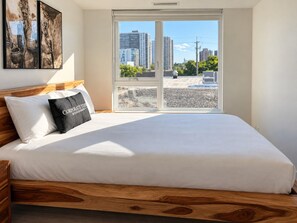 Ein Schlafzimmer mit einem großen Bett, einem Fenster mit Blick auf die Stadt und einem Holzkopfteil.