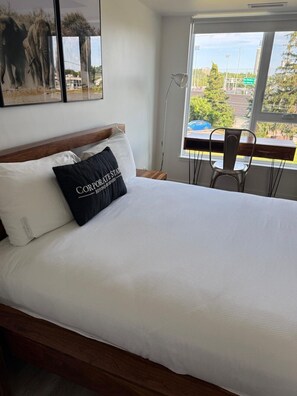 Ein Hotelzimmer mit einem großen Bett, einem Fenster mit Blick auf eine Stadtlandschaft und einem Sessel am Fenster.