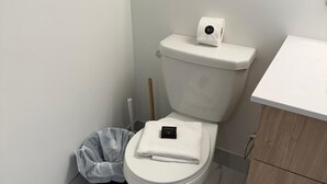 Une salle de bain équipée de toilettes, d’une poubelle et d’un meuble en bois.